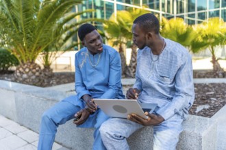 Two senegalese businessmen wearing traditional dashiki attire are discussing business while using a