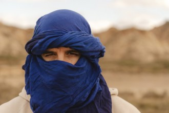 Portrait of a tuareg man adorned in an indigo tagelmust, set against the vast, arid landscape of