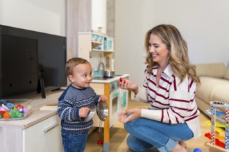 Happy mother and baby boy playing with toy kitchen set in living room, enjoying quality time
