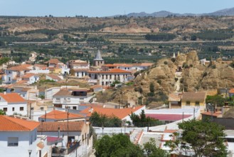 Panoramic view of a village with red roofs and mountains in the background under a clear sky, cave