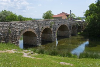 Stone bridge over river, flanked by green bank and small building, Bridge over the river Zrmanja,