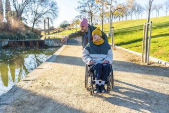 Man pushing friend in wheelchair, enjoying a sunny day in the park, surrounded by nature, trees,