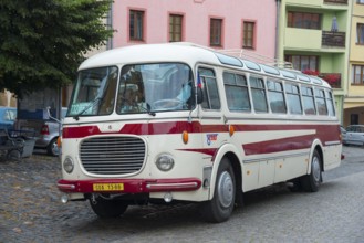 A classic old bus on a cobbled street in a town with colourful buildings, vintage car, Skoda 706