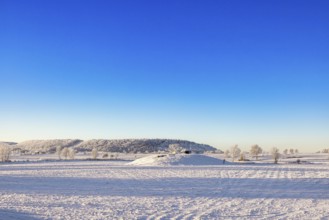 Winter landscape with snow and frost in the countryside with a Passage grave on a hill and a table