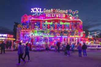 Colourfully illuminated fun house at a funfair at night with numerous visitors, Cannstatter Wasen,
