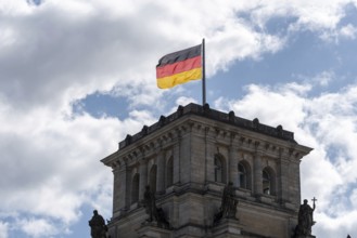 A German flag flies over a building tower of the Reichstag against a cloudy sky, Berlin, Germany