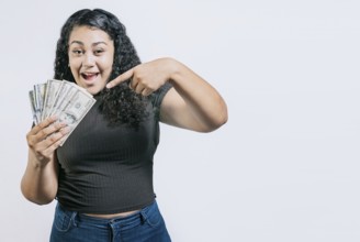 Smiling young woman holding and pointing money isolated. Attractive latin girl holding and pointing