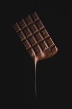 A floating chocolate bar with melting drops on a black background