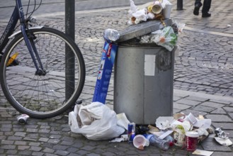 Overfull rubbish bin with trash around and garbage piled on top in city street