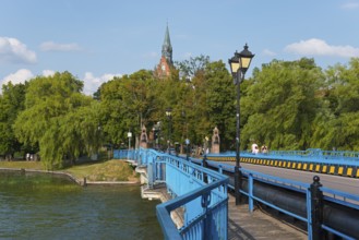 Blue bridge against a lush green backdrop with church tower and lanterns in sunny weather, historic