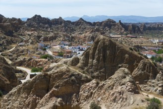 A small village nestled in a rocky, rugged landscape under a sunny sky, view from the Mirador del