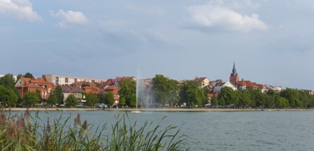 Panorama of a lakeside town with church tower and trees, central fountain, summer scenery, Elk,