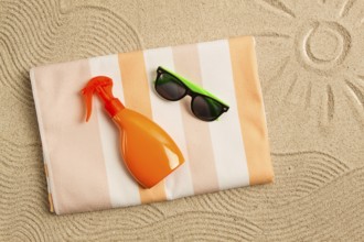Drawing on the sand, sun and waves, sunglasses, with an orange bottle, beach towel, sun spray, on