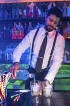 Professional bartender preparing cocktails, pouring alcoholic beverage into glasses with ice at bar