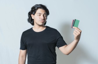 Unsure guy holding a credit card isolated. Confused man holding and looking at credit card