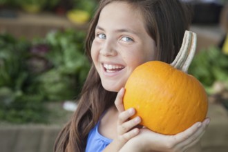 Happy young blue eyed girl holding a fresh pumpkin at the farmers market