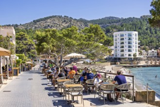 Outdoor restaurant with people on a pedestrian street in a coastal village by the beach with hotels