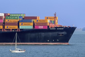 Sailboat sailing past bow of container ship, containership Hudson Express of the Hapag-Lloyd AG