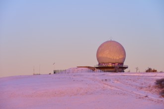 A radar station radome on a snow-covered hill at sunset with pink sky, winter, Wasserkuppe,