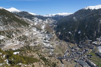 Verschneite Berge und ein Tal mit Straßen und verstreuten Gebäuden unter einem klaren blauen Himmel