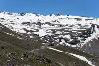 Snow-covered mountains under a bright blue sky with rocky landscape in the foreground, view of
