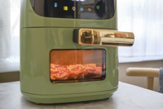 A fresh pork chop is being cooked in an air fryer, showcasing its sleek green design. The appliance