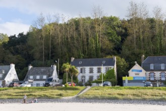 Beach view with houses and shops on the coast, surrounded by green trees, Plage Saint Efflamm,