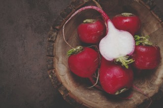 Fresh red radishes are displayed on a rustic wooden cutting board, highlighting their smooth skins