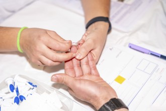 Close-up of a nurse checking blood sugar level by pricking the finger of a blood donor