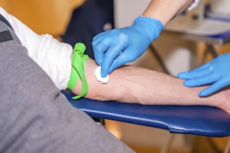Nurse cleaning the area she is going to prick on the arm of a blood donor using a cotton swab