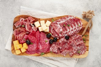 Assorted, sliced meat appetizer, prosciutto, salami and ham, with cheese and olives, on a wooden