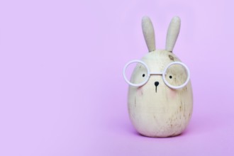 Cute funny egg shaped Easter bunny with glasses on pink background with copy sapce