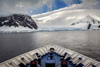 The view from the bow of a ship shows majestic mountains under a dramatic sky, cruise ship underway