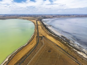Aerial photo contrasting vibrant green and gray lakes divided by roads and golden fields in