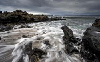Waves blaze on the beach, rocky coast with volcanic stones, long exposure, Playa de la Pequeña,