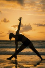 A serene silhouette of a woman practicing yoga on a beach during sunset in Tulum, Mexico. The warm