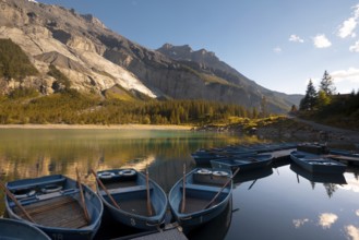 A serene view of Oachinensee in Switzerland captures several blue boats docked on the calm lake,