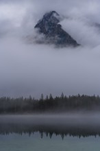 A stunning view of a mountain peak in Hintersee, partially shrouded in fog, surrounded by serene
