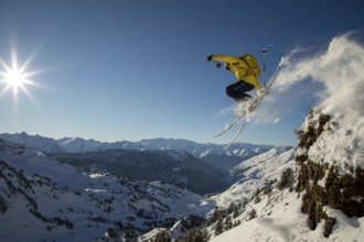A skier in a yellow jacket performs an exhilarating jump off a snowy cliff, surrounded by a