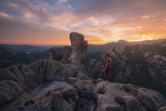 Back view of unrecognizable man standing on rocky outcrop, gazing at vibrant sunset over Pedriza
