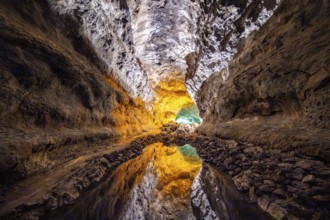 Lava tunnel, illuminated lava cave with perfect reflection in an underground lake, Cueva de los