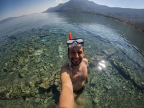 A man enjoys snorkeling in Greece, exploring the crystal-clear waters and rocky seabed. The scenic