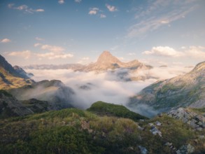 Serene mountain peak rises above a lush green landscape enveloped in wispy clouds under a vast blue
