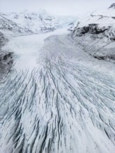Aerial view of Icelandic winter landscape featuring a vast, icy glacier with intricate patterns.