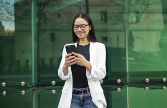 Hispanic businesswoman wearing glasses and a white blazer, smiling while using her smartphone