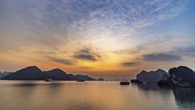 Wide sky at sunset over still water and distant rocks, sunset in Halong Bay, Vietnam