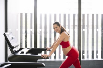 Pregnant woman in a red sports outfit exercising on a treadmill, promoting pregnancy wellness and