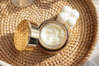 A luxurious skincare cream in an elegant gold jar, placed on a woven rattan tray beside a white