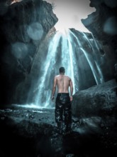 Adventurous young man under Gljufrafoss waterfall in winter in Iceland
