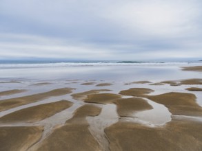 Serene coastal landscape featuring expansive sandy shores and reflective tidal pools under a cloudy